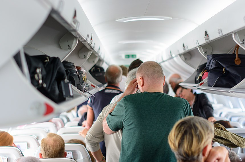 Pessoas em pé no interior de aeronave organizam as malas durante embarque