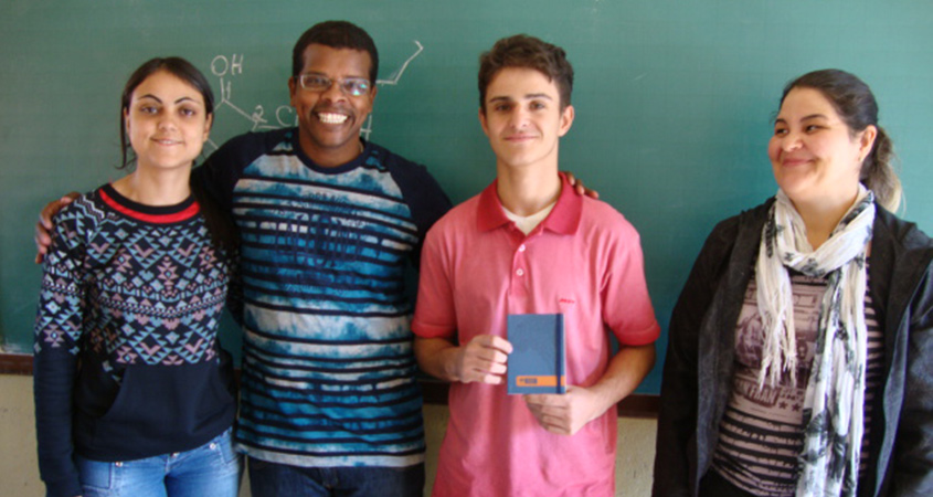 Diretor e as professoras de português e biologia premiam aluno com caderno do Jovem Senador