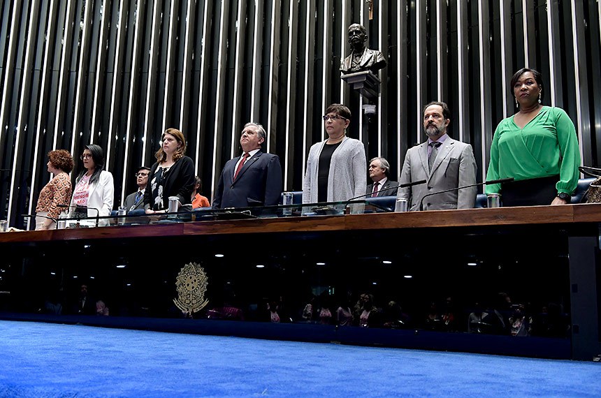 Plenário do Senado Federal durante sessão especial destinada a comemorar o Dia Internacional da Não-Violência Contra a Mulher. Em posição de respeito, parlamentares e convidados acompanham o Hino Nacional do Brasil executado pela banda do Centro de Ensino Fundamental nº 11. Mesa: representante do Ministério da Mulher, da Família e dos Direitos Humanos e coordenadora-geral do Programa Mulher Viver sem Violência, Valéria Laval; presidente e fundadora do Instituto Mulheres Feminicídio Não (AME), Lúcia Erineta; diretora-geral do Senado Federal, Ilana Trombka; presidente e requerente desta sessão de comemoração, senador Izalci Lucas (PSDB-DF); presidente nacional do Conselho de Mulheres Cristãs do Brasil (CMCB), Patrícia Óliver; juiz e coordenador do Núcleo Permanente Judiciário de Solução de Conflitos e Cidadania da Mulher em Situação de Violência Doméstica e Familiar do Distrito Federal do Tribunal de Justiça do Distrito Federal e Territórios (NJM/TJDFT), Ben-Hur Viza; delegada-chefe da 6ª Unidade Policial do Paranoá, Jane Klébia. Foto: Waldemir Barreto/Agência Senado