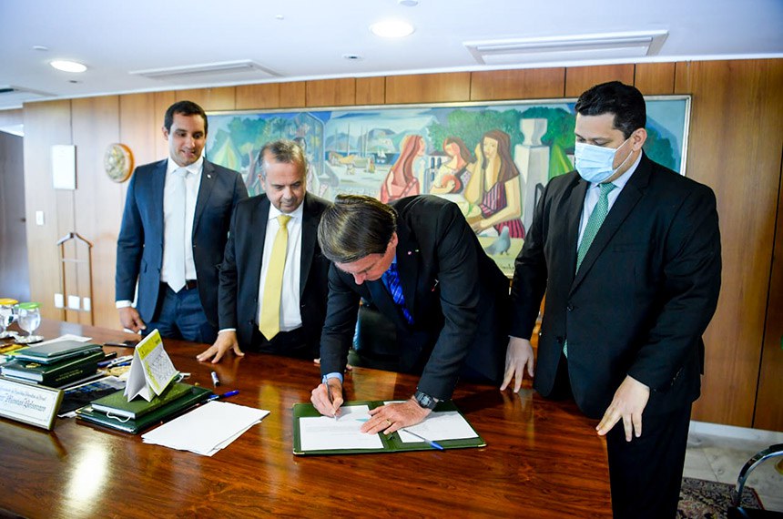 De máscara, o presidente do Senado, Davi Alcolumbre, observa o presidente Jair Bolsonaro assinar a nova lei