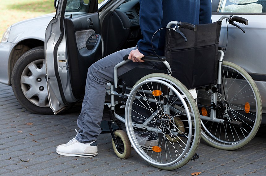 Homem em cadeira de rodas próximo a seu carro. Carro adaptado para portadores de necessidades especiais.