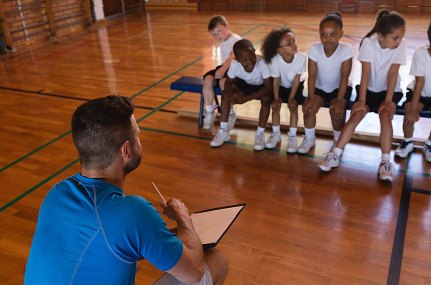 Basketball coach talking with schoolkids at basketball court in school