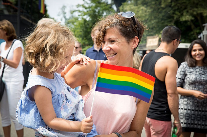 Amsterdam, the Netherlands - July 23, 2016: young mother with her daughter in her arms waving a rainbow flag during Pink Saturday celebration in Vondelpark for 2016 Gay Euro Pride