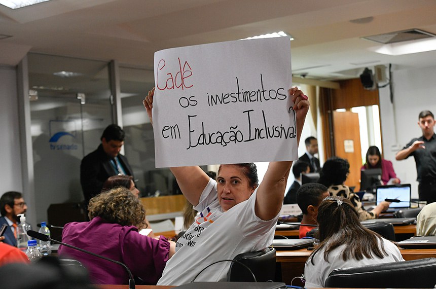 Convidada exibe cartaz que diz: "Cadê os investimentos em Educação Inclusiva? ".