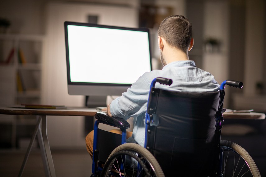 Vista traseira do empresário deficiente sentado em uma cadeira de rodas na mesa em frente ao monitor do computador e concentrando-se no trabalho.