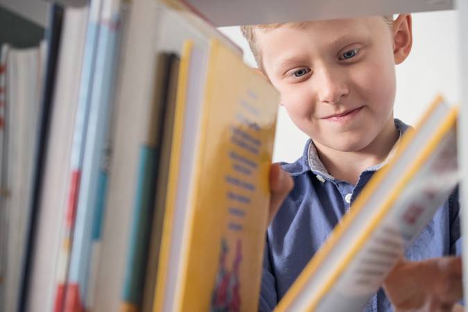 Cute little boy choose a book on the bookshelf