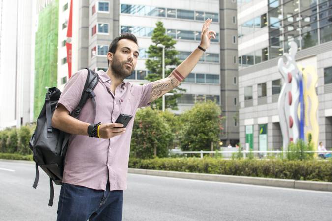 A young white italian man with tattoos, hailing a taxi whilst holding a cellphone in Tokyo.