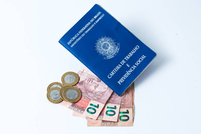 Brazilian work document and social security document (carteira de trabalho) with money as a concept of how little money the worker made  on white background -