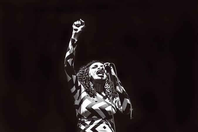 Teresa Cristina cantando com o punho erguido. A foto é em preto e branco.