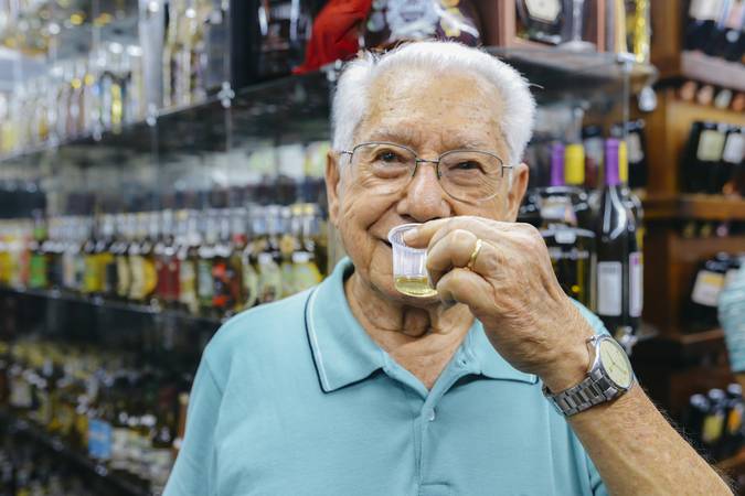 Belo Horizonte, Brazil - Dec 23, 2017: Older man 80-90 samples a type of cachaca drink, made from distilled rum, before purchasing at the Mercado Central in Belo Horizonte