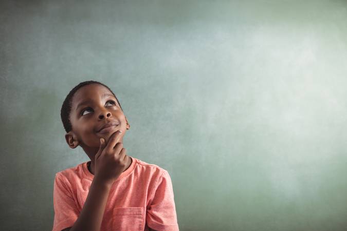 Thoughtful boy standing against greenboard in classroom