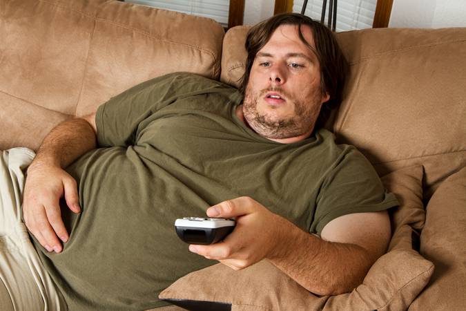 Overweight guy sitting on the couch with remote in hand trying to watch some TV.