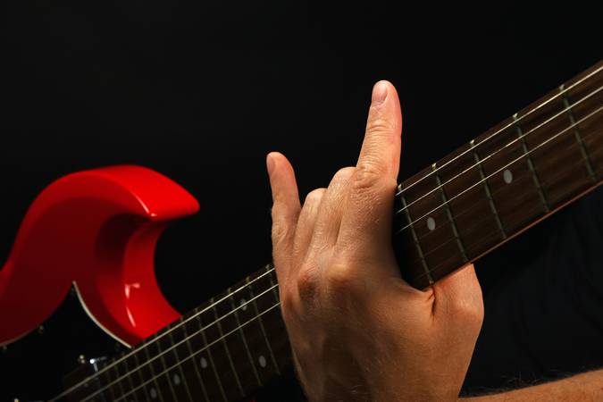 Hand with red guitar and devil horns isolated on black