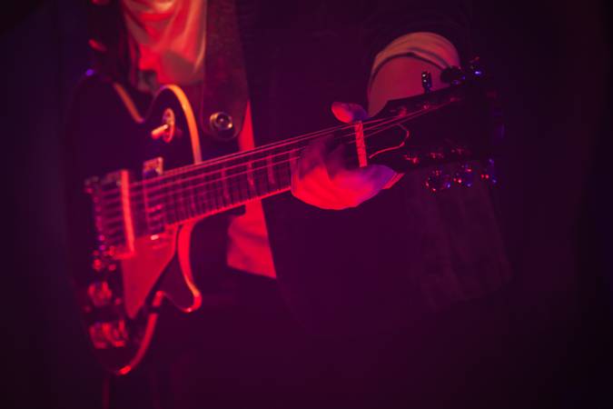 Electric guitar player on a stage with red scenic illumination, soft selective focus