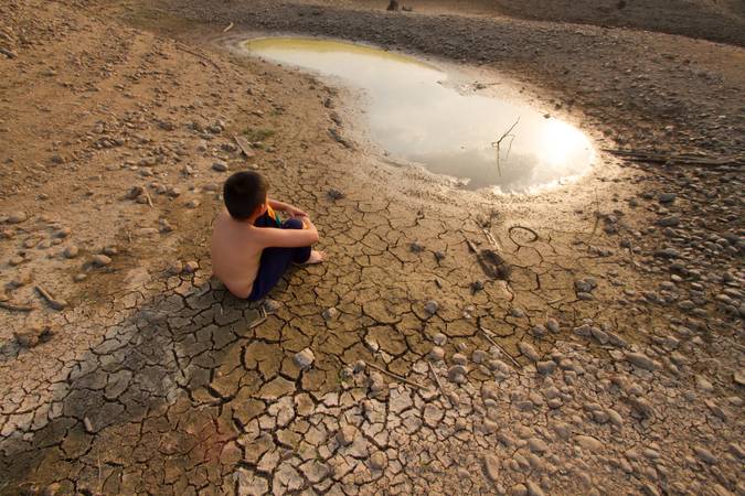 Child sit on the cracked earth and looking to the last pond on the lake. Metaphor for Global warming and Climage change.
