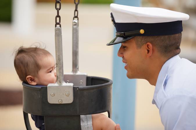 Image of a military man in uniform playing with his baby in the park