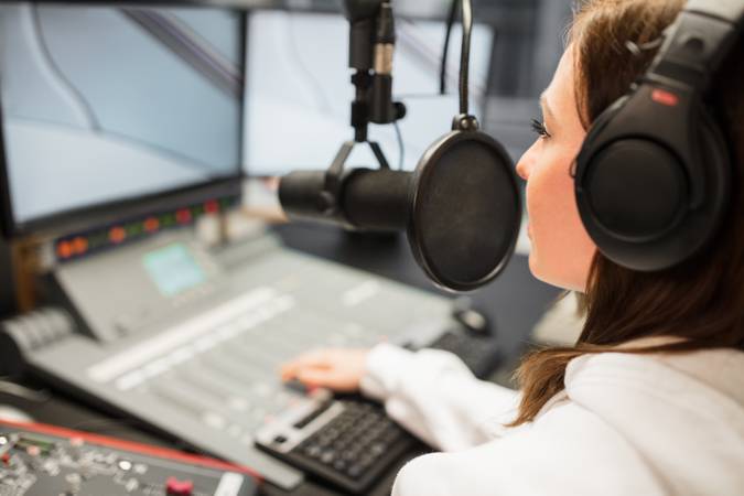 Young female jockey wearing headphones while using microphone in radio station