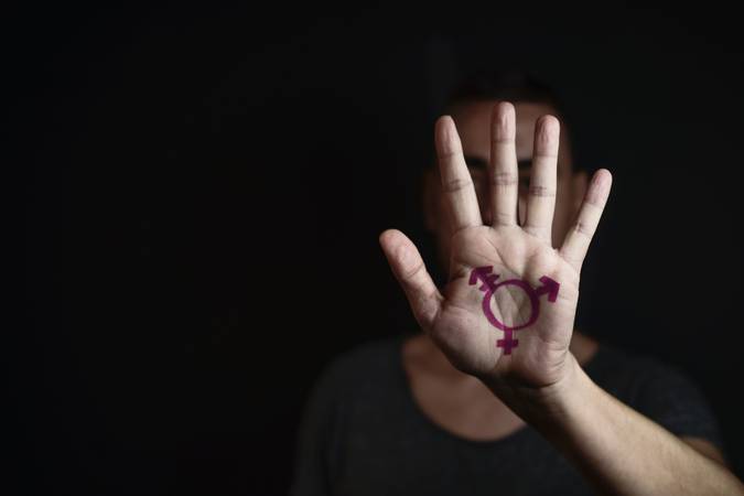 closeup of a transgender symbol painted in the palm of the hand of a young caucasian person against a black background, with a negative space on the left