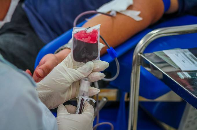 Imagem do braço de homem doando sangue enquanto enfermeira segura bolsa de sangue.