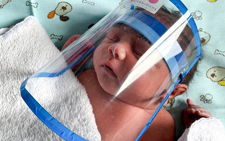Imagem de recém-nascido com viseira de proteção contra o novo coronavírus.