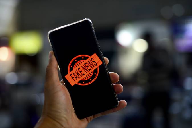 mão segurando celular que exibe uma imagem com o texto fake news em vermelho.