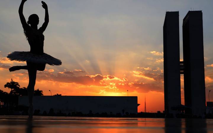 bailarina dançando, na Praça dos Três Poderes, contra a luz do pôr do sol e com as torres do Congresso Nacional ao fundo.