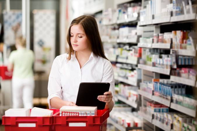 Farmacêutica segura tablet enquanto confere remédios em uma farmácia.