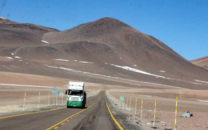 Caminhão em estrada com os Andes ao fundo.
