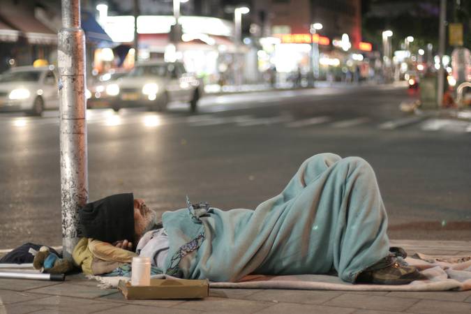 Pessoa em situação de rua dormindo numa esquina.