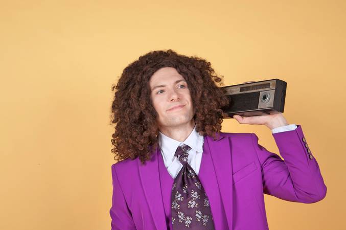 Caucasian man with afro wearing Purple Suit listening to music